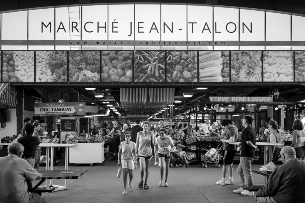 Three girls walking away from busy outdoor market. 
