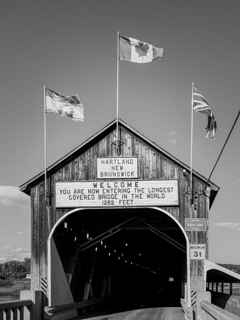Welcome sign located on bridge with three flags blowing in the wind. 