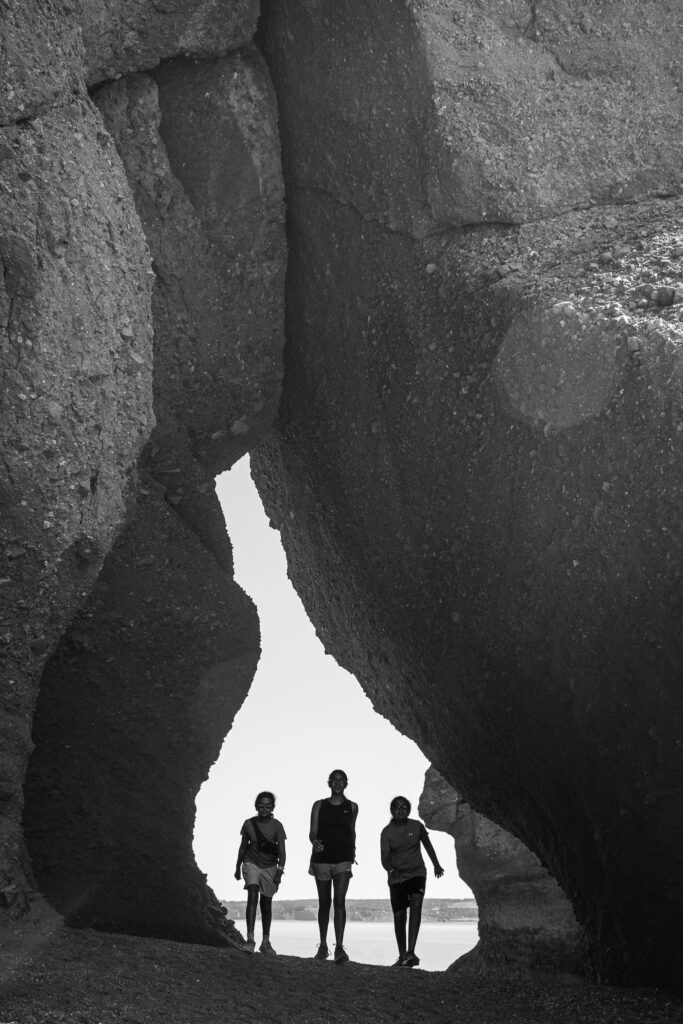 Three girls walking through a gap in large rock formation.
