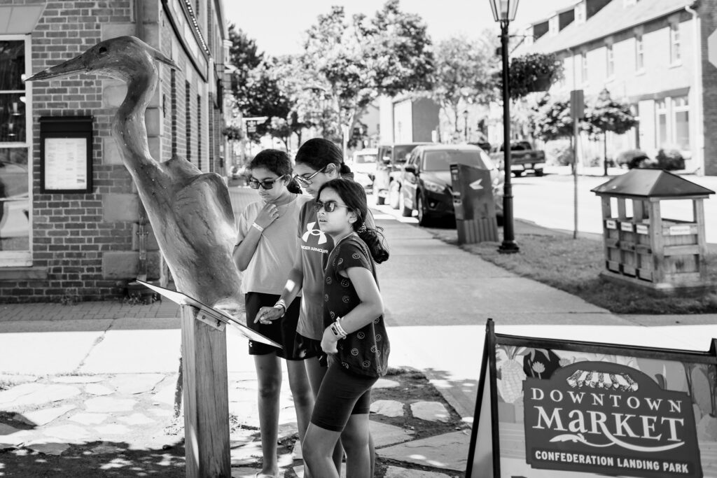 Three girls looking at sign standing next to a large bird statue. 