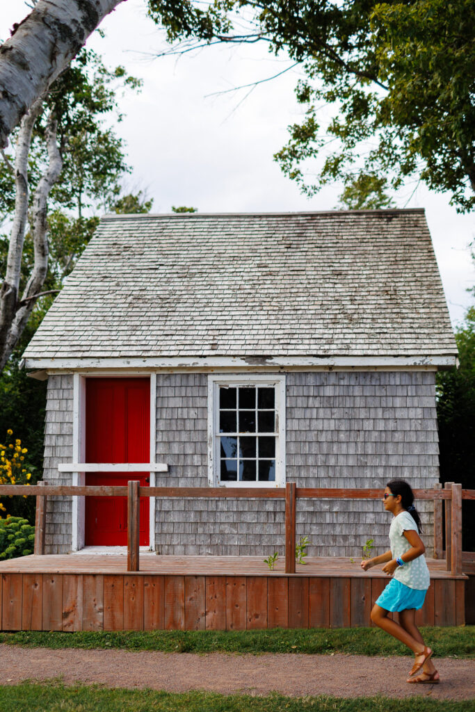 Girl running on a red path by a house with cedar shakes. 