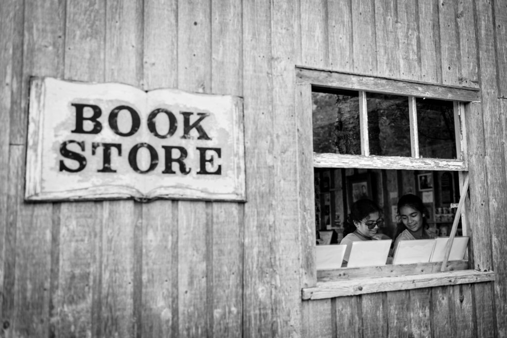 Two kids through the window of a book store. 