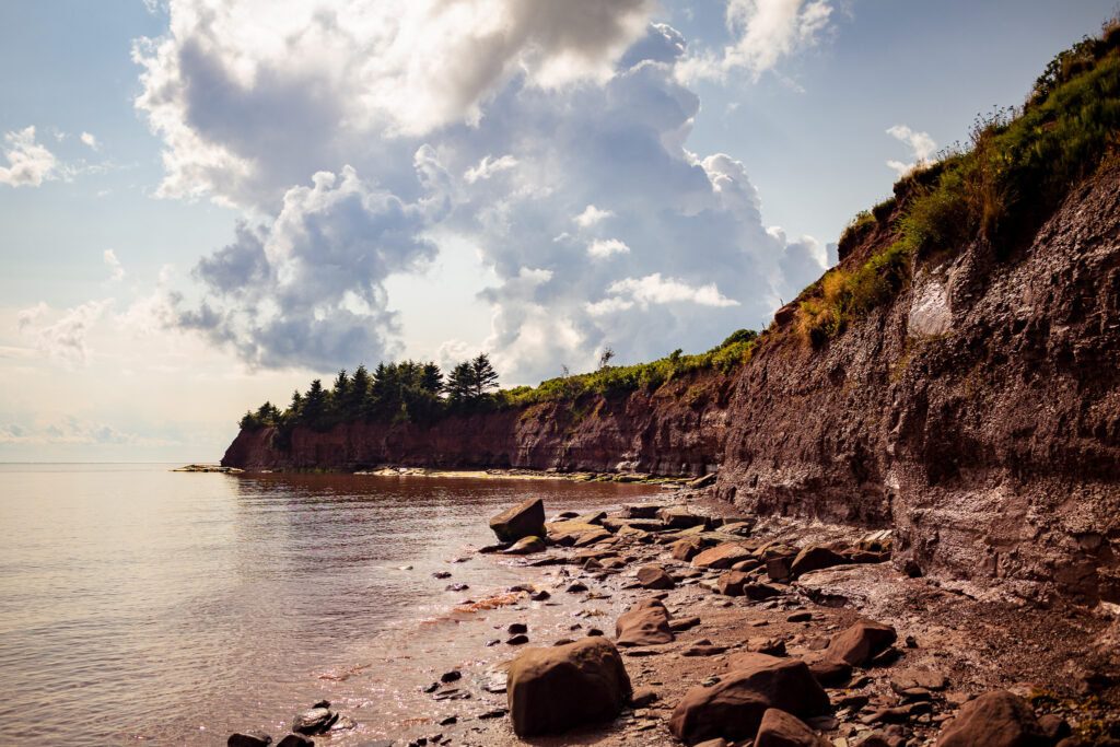 Rocky red coastline with cloud filled sky. 
