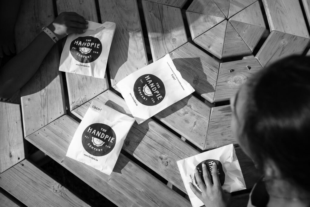 Kids grabbing for packages labeled The Handpie Company from a table. 
