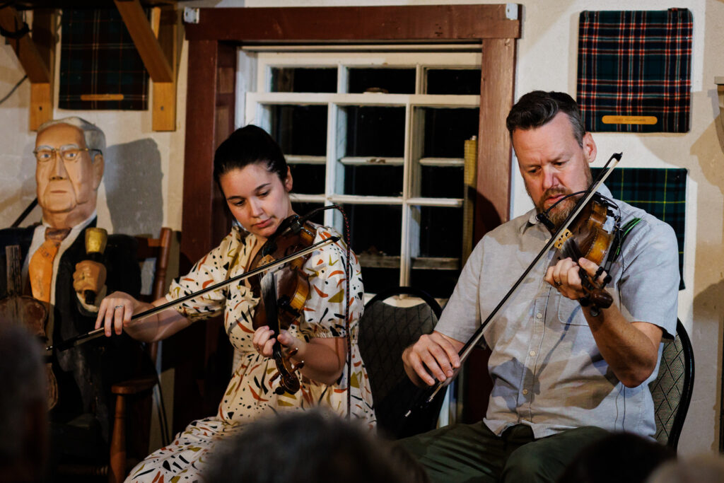 Two fiddlers performing for a crowd. 