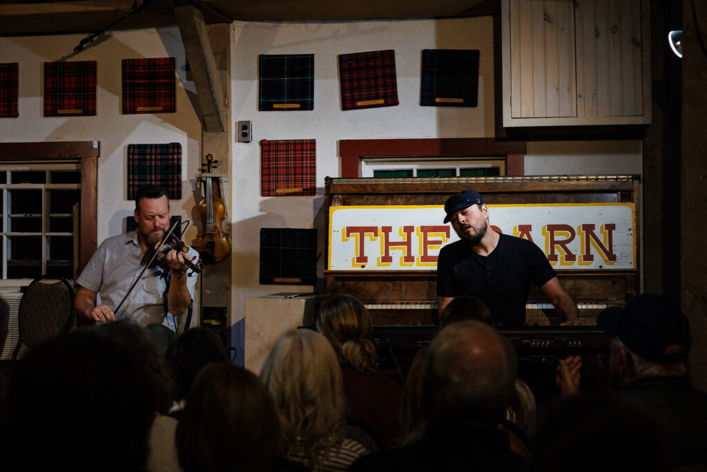 One fiddler and a pianist performing for a crowd.