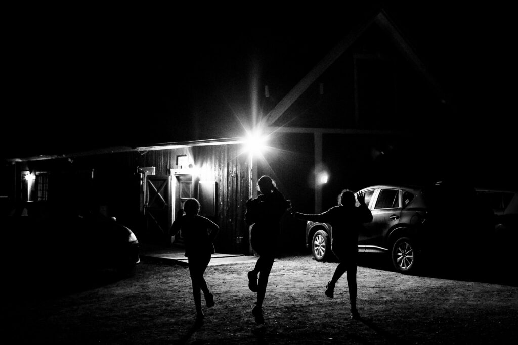 A silhouette of three kids skipping by a barn. 