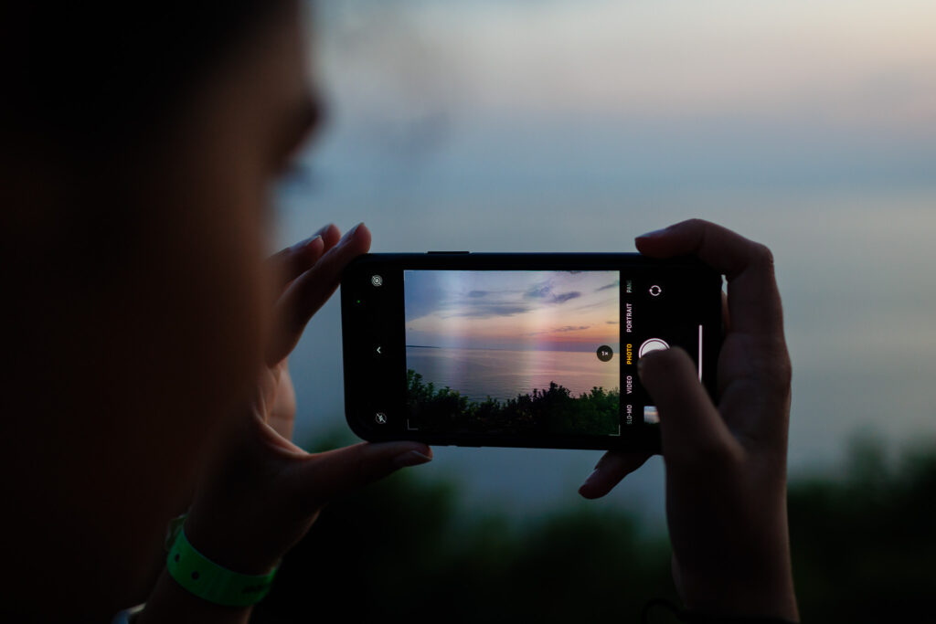 Girl holding an iPhone taking a picture of the sunset. 
