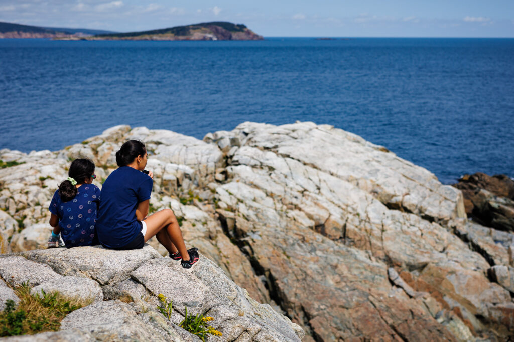 Two kids sitting on a rocks while looking at the ocean. 