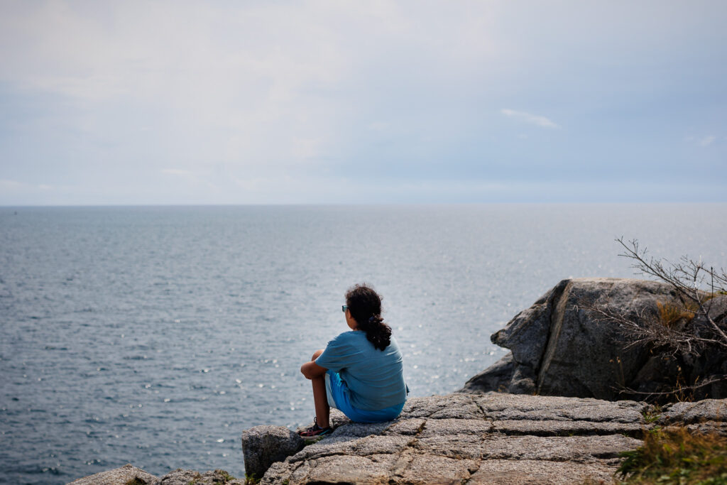 Girls sitting on a rock while looking at the ocean. 