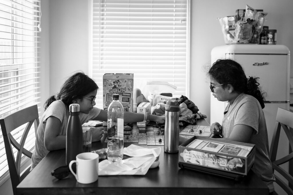 Two kids playing a board game on a table top cluttered with various items in Sydney Nova Scotia. 