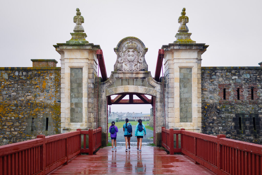 Three kids walking across a red bridge into the Fortress of Louisbourg. 
