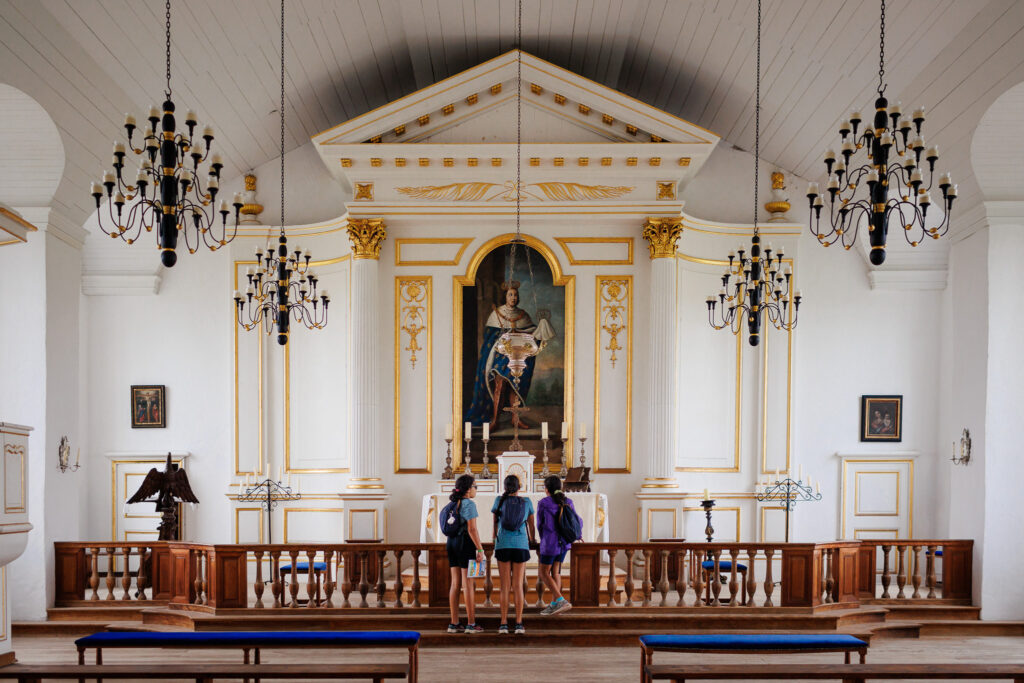 Three girls looking at the church with gold trim and black chandlers located at the Fortress of Louisbourg.