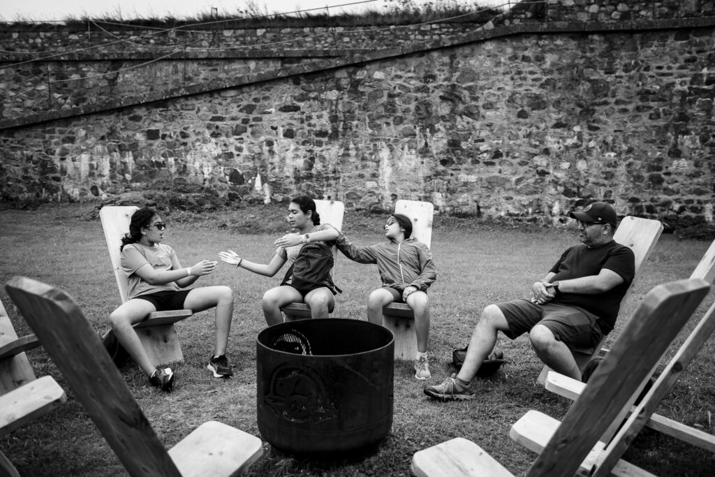 Three kids and their father sitting on chairs playing a hand slap game. 