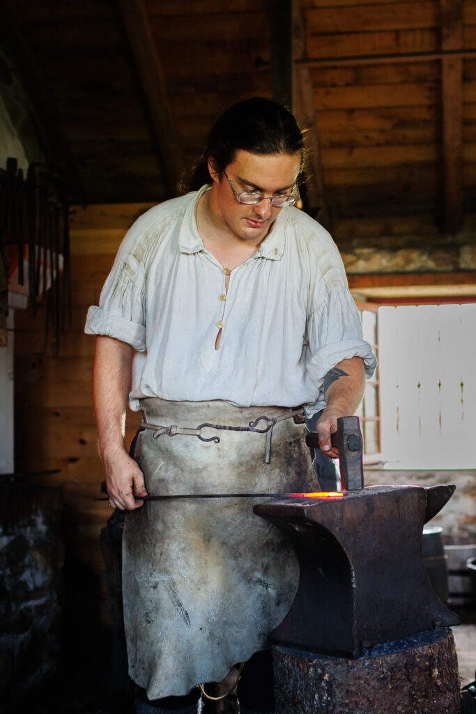 Blacksmith using a metal hammer on a red hot poker to make a belt hook. 