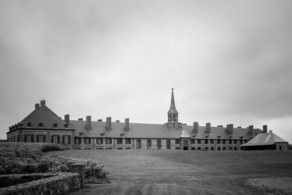 Large stone building with a steeple with a large area of grass in the foreground. 