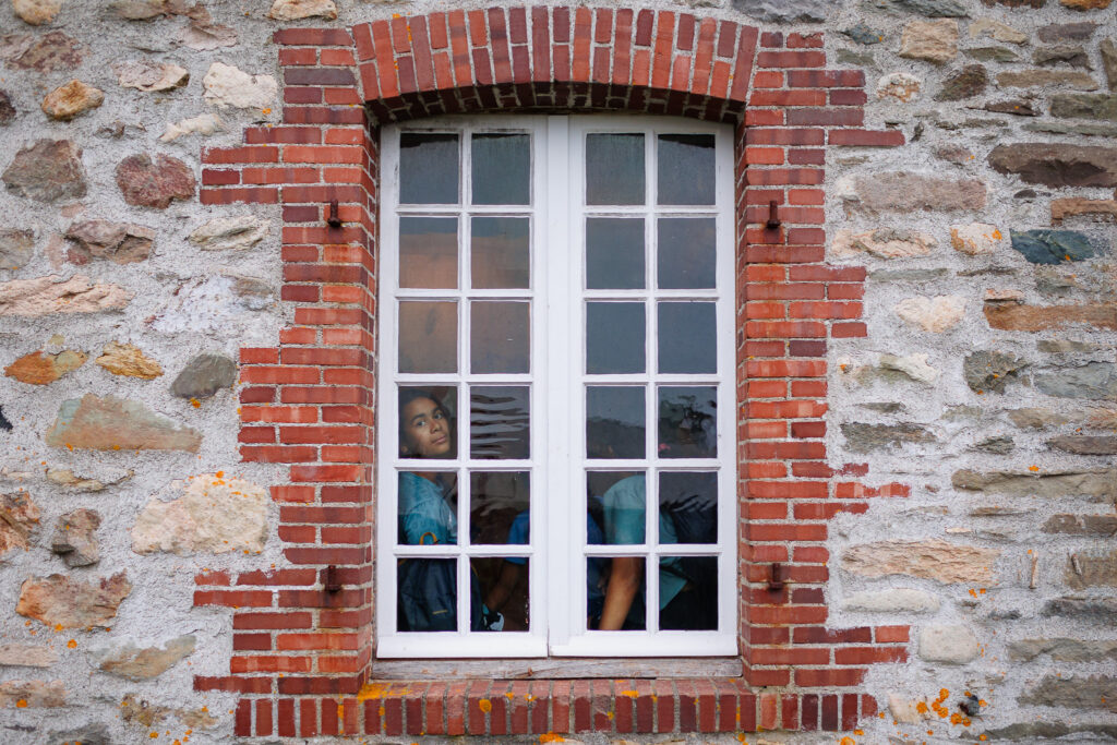 Girl looking through a panelled window with a red brick frame on a stone building. 