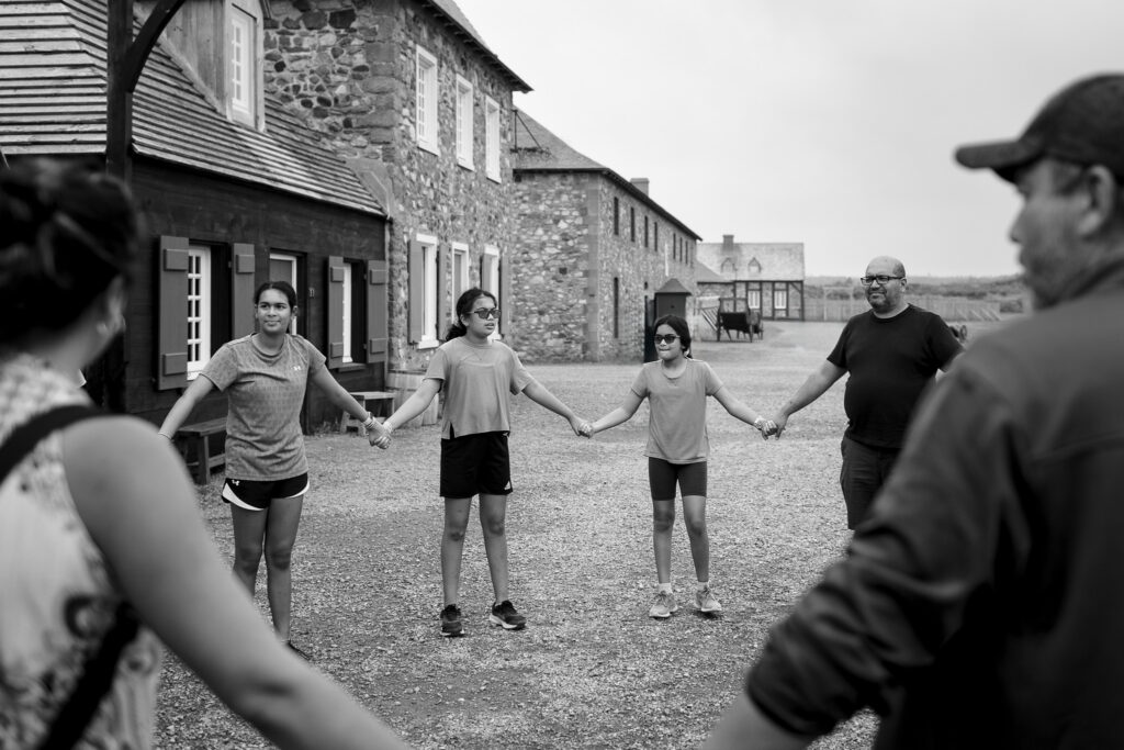 Three girls and their father holding hands in a circle listening to instructions on the group dance. 