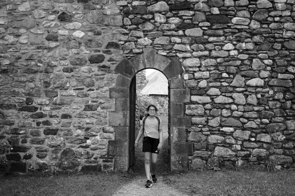 Girl walking through an arched doorway on a stone building. 