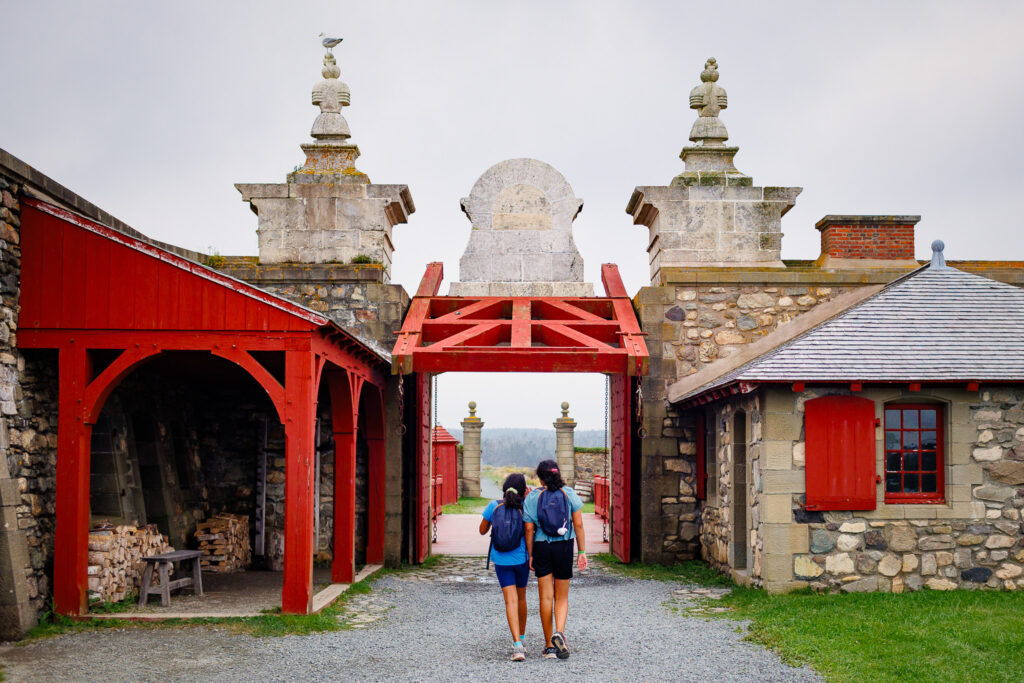 Girls walking through red archway of Fortress of Louisbourg. 